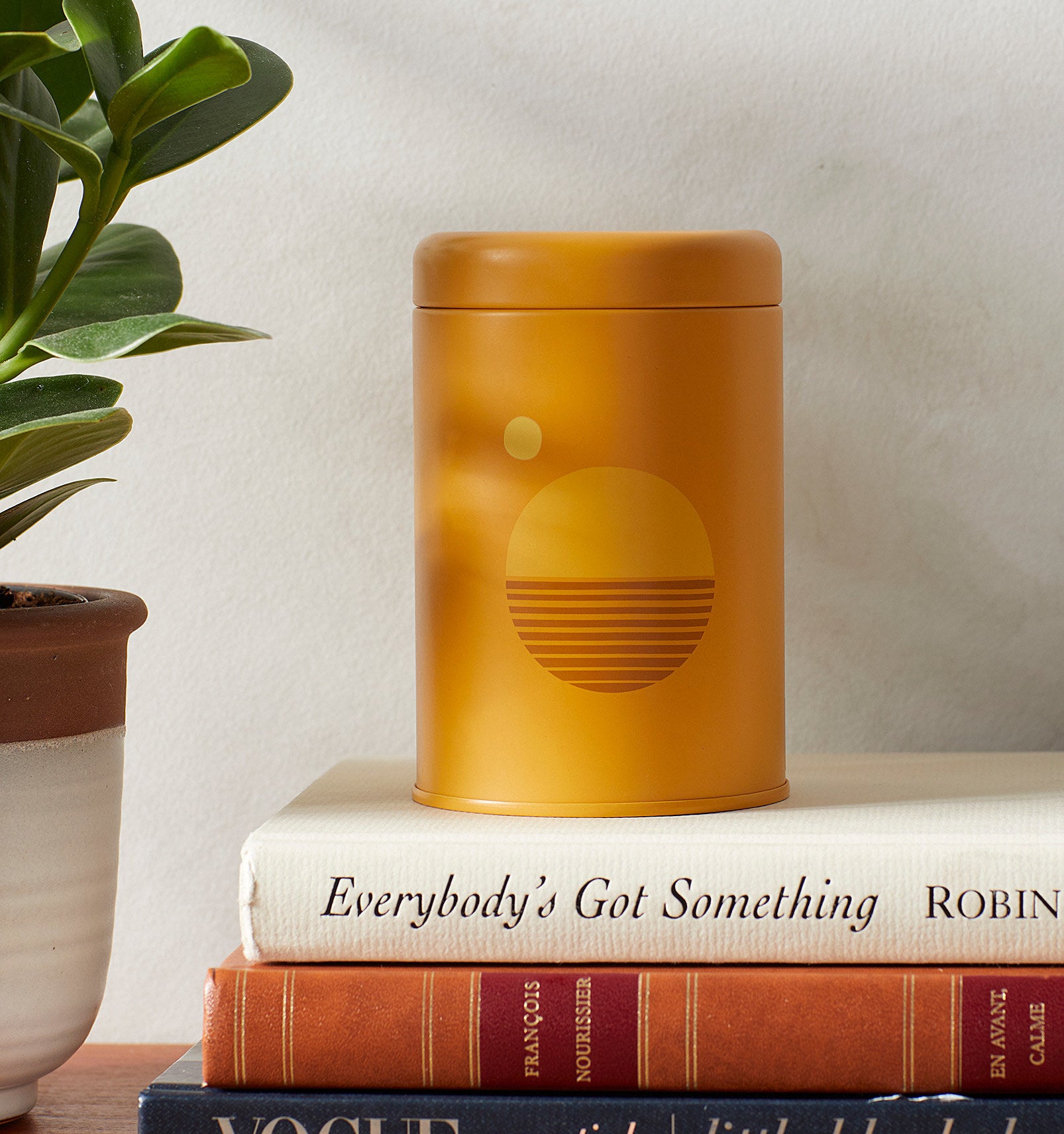A candle in a small tin jar on a stack of books