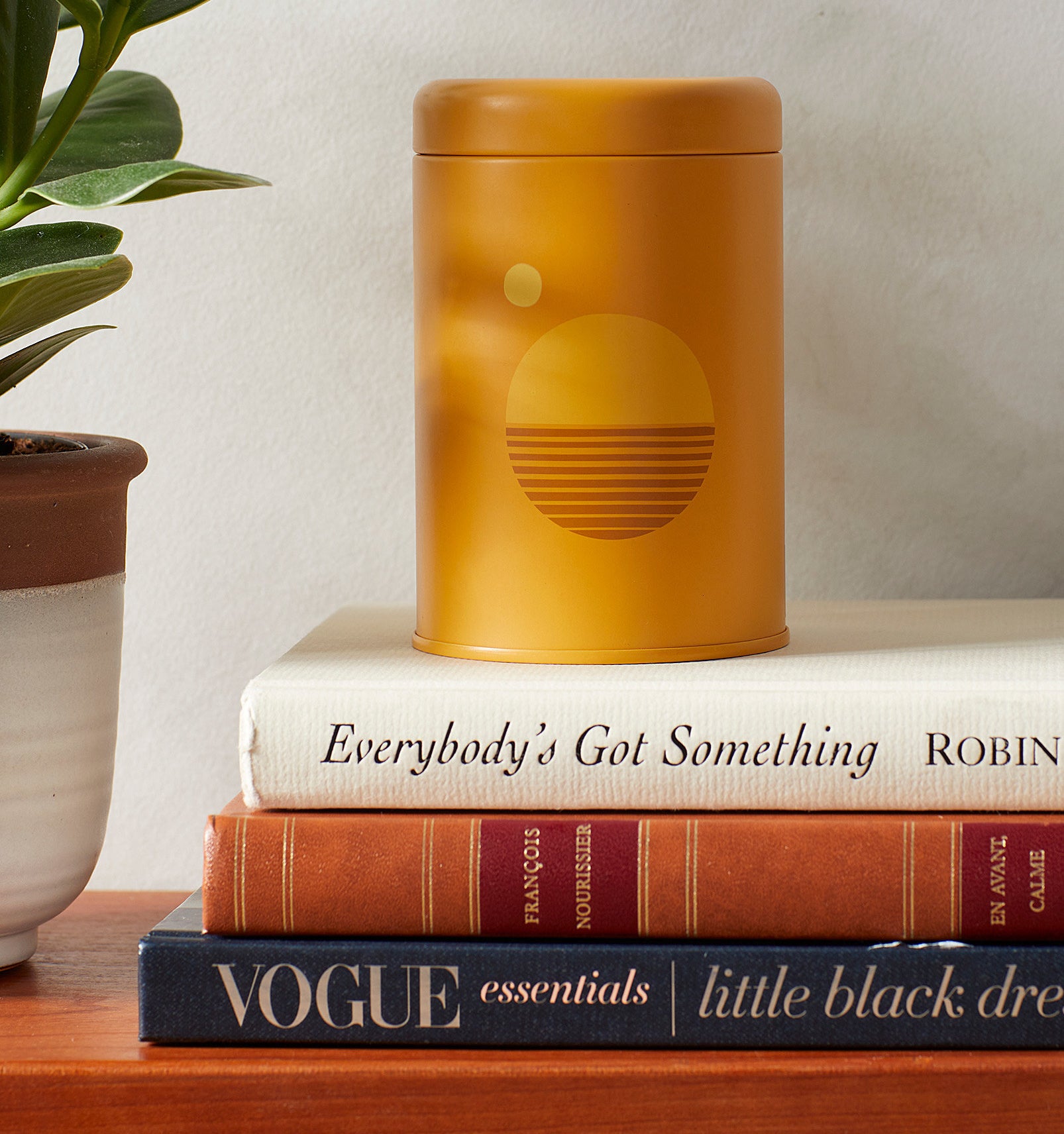A candle in a small tin jar on a stack of books