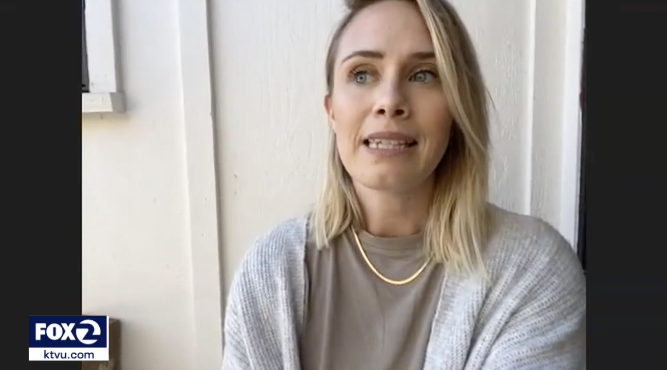 A blonde woman wearing a cardigan and gold necklace speaks to the camera