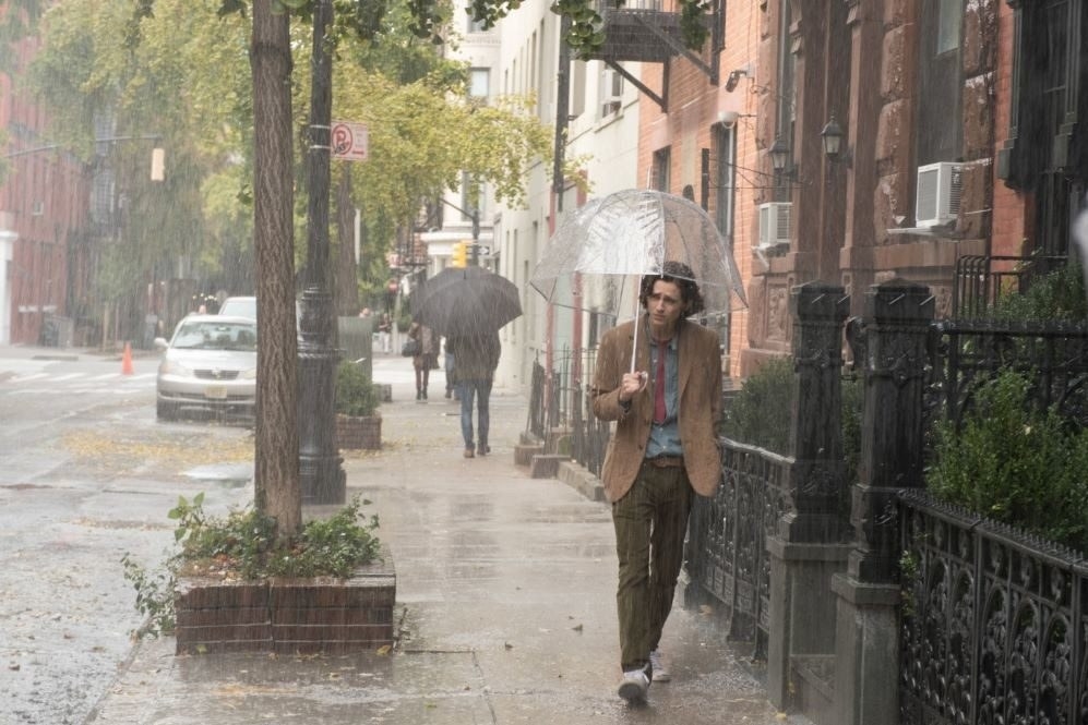 A boy walking through a city holding an umbrella as it rains around him