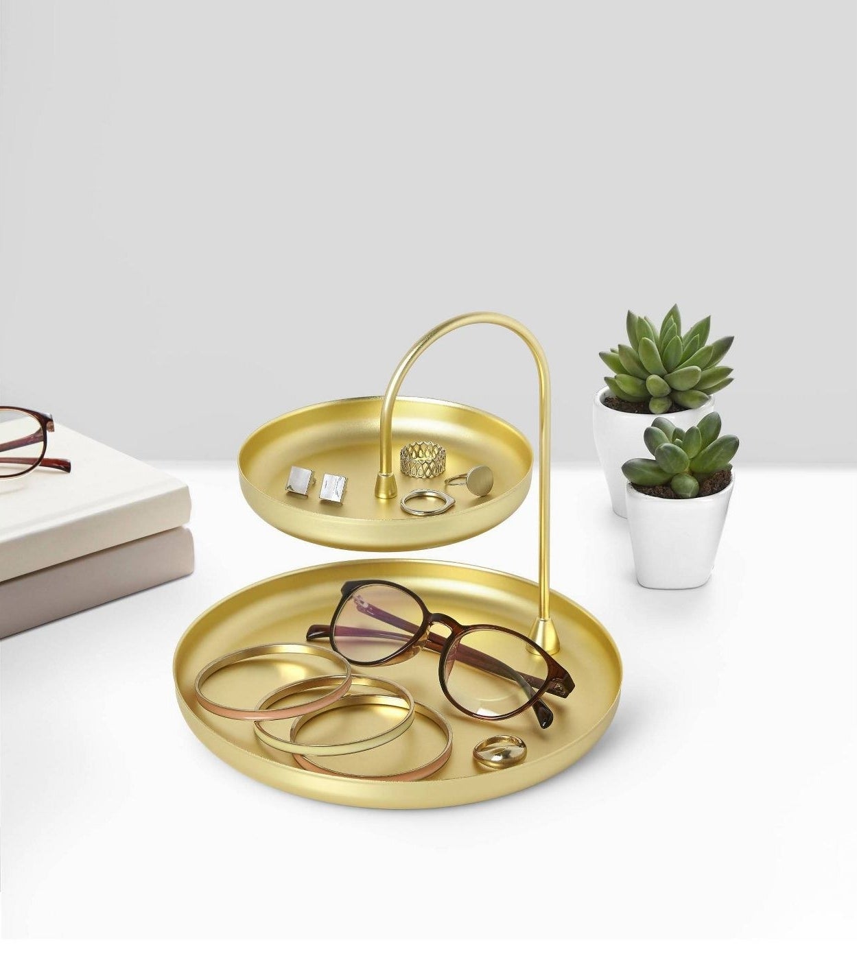 Brass two-tier tray displaying brown glasses, yellow, pink, and orange bracelets and gold rings.