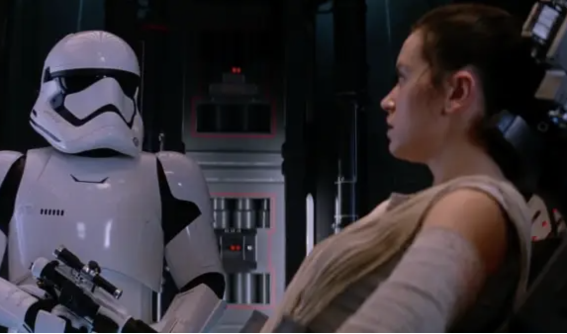 A stormtrooper stands over a captive Rey 