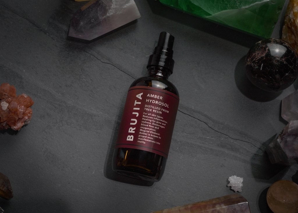 Dark brown bottle of Brujita Skincare&#x27;s Amber Hydrosol next to crystals