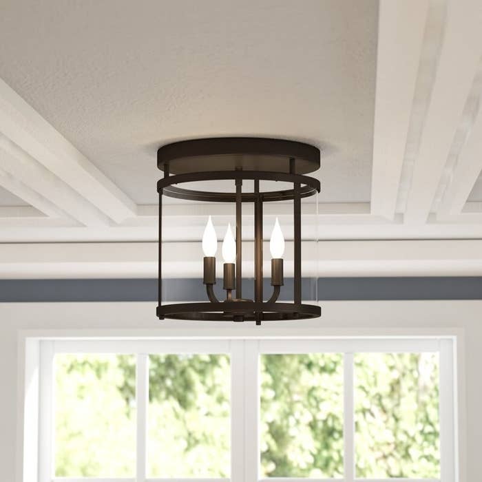 The light, which is cylindrical glass with a dark bronze frame, and a base with three narrow bulbs extending from it