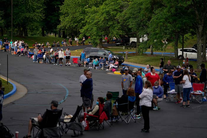 A huge queue of people, many of them sitting in folding chairs, snakes around a street