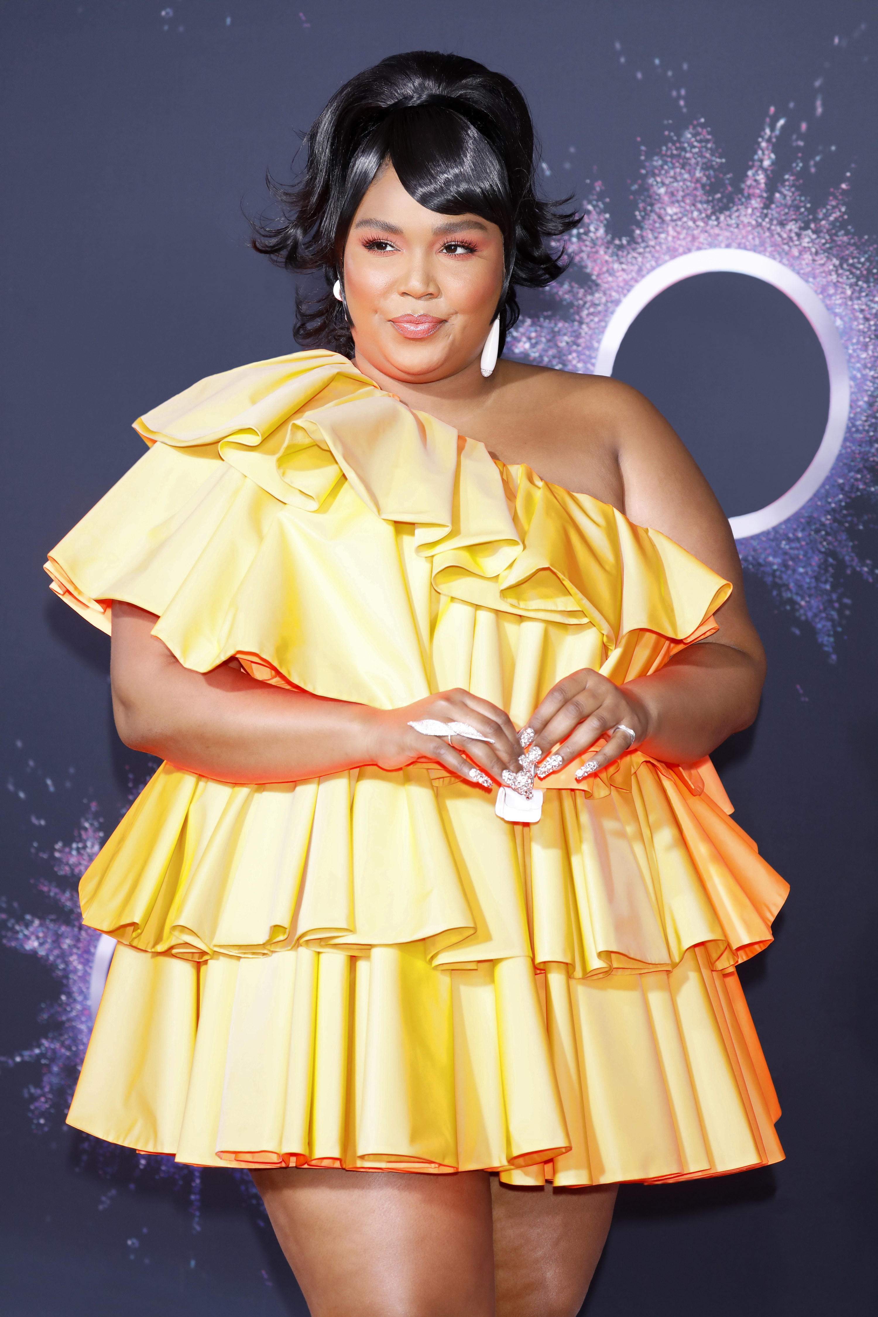 Lizzo wears a brightly colored dress and holds a tiny purse with both hands