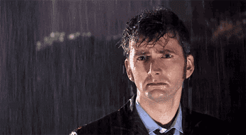 The 10th Doctor (David Tennant) stand in the rain with a solemn look on his face in &quot;Doctor Who&quot;