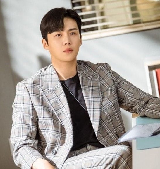 A close up of Han Ji-pyeong; he is wearing a tweed suit with a black t-shirt