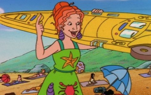 Ms Frizzle holds the school bus in the shape of a surfboard at the beach