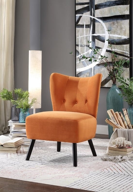 The chair in orange, which has black splayed wooden legs, no arms, and a button-tufted back