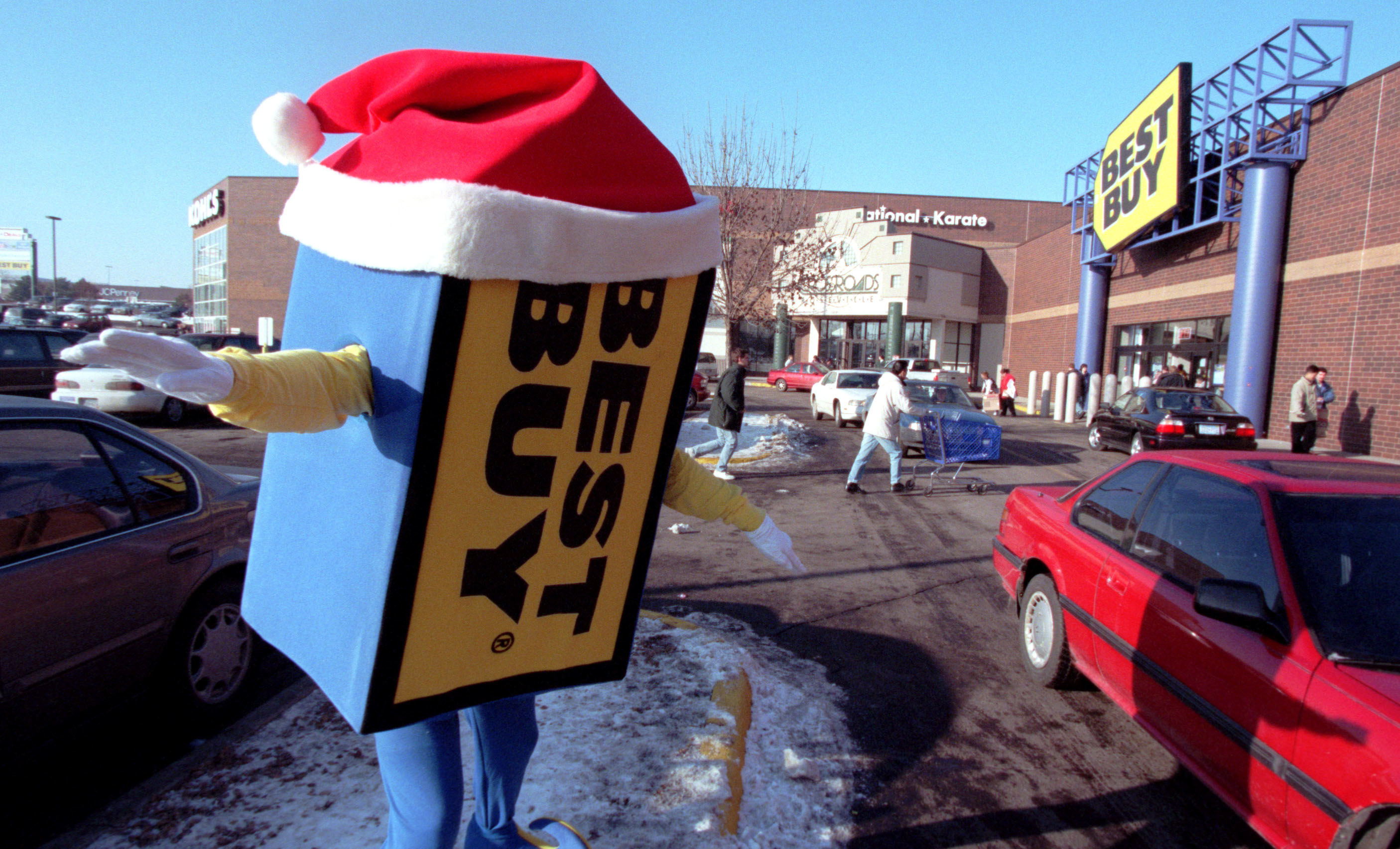 The Best Buy mascot dancing in a parking lot with a Santa hat on 