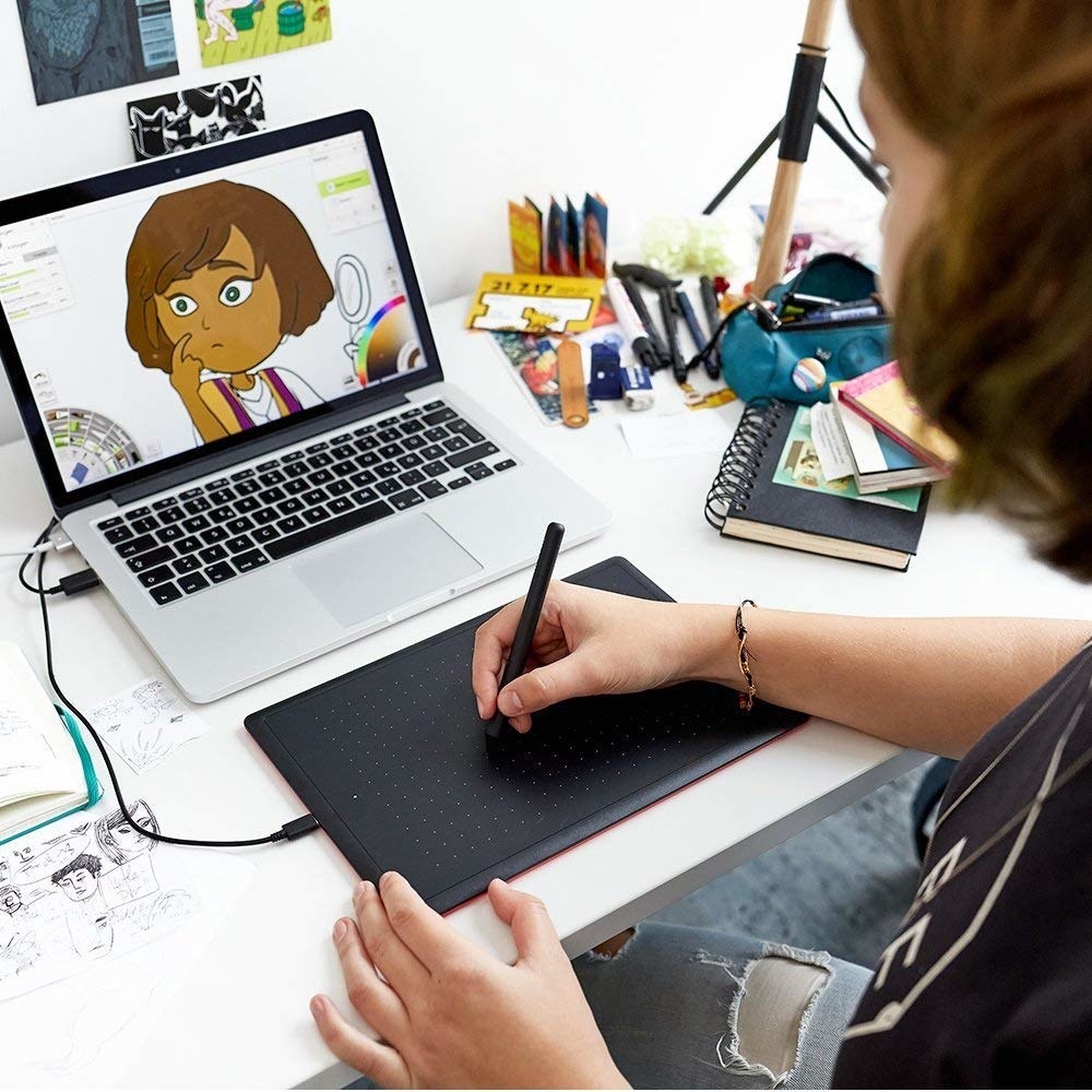 A person drawing on their tablet, connected to their laptop.
