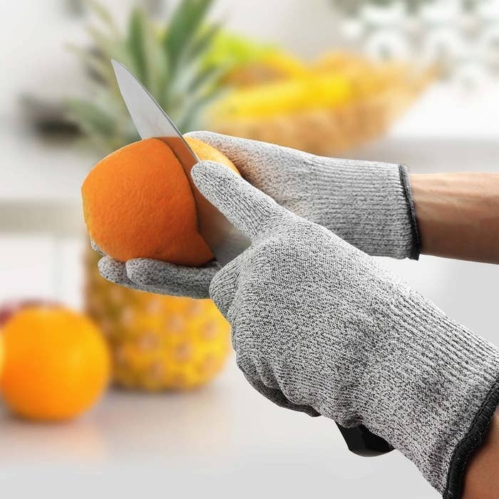 A person cutting an orange with the cut-resistant gloves on