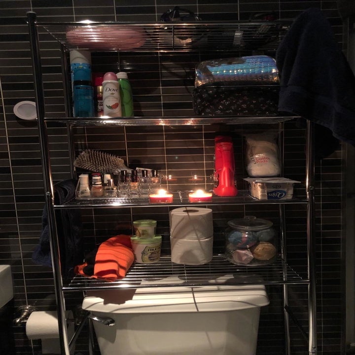 reviewer photo showing over-toilet storage shelf with several products and candles on it 