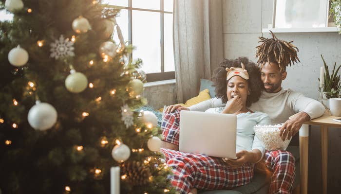 A couple sits on a sofa to watch a movie in their home decorated for Christmas