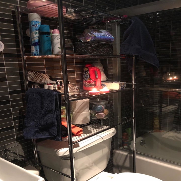 reviewer photo showing over-toilet storage shelf with several products and candles on it from a different angle 