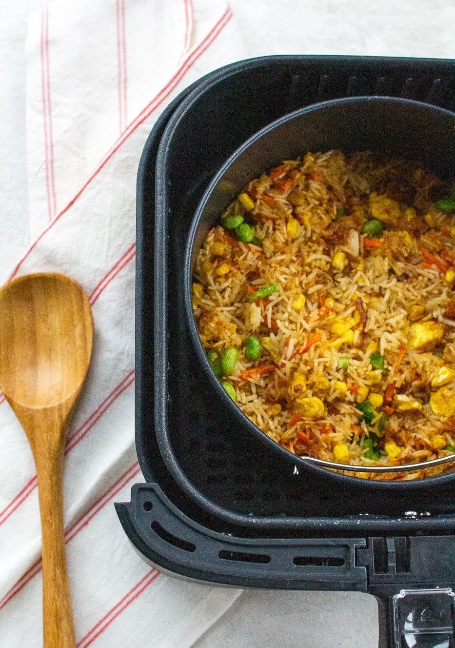 Fried rice cooking in a baking dish in the basket of an air fryer.