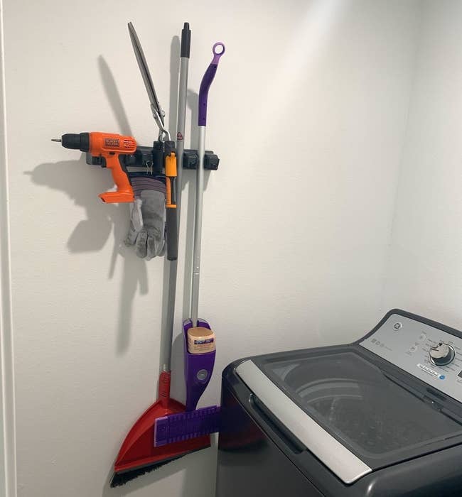 reviewer photo showing the organizer with a broom, Swiffer, and even a drill attached to it 