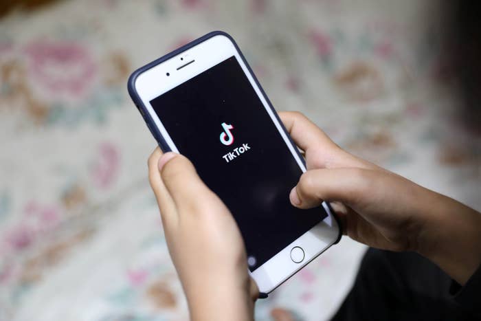 Two hands hold a phone that is displaying the TikTok app