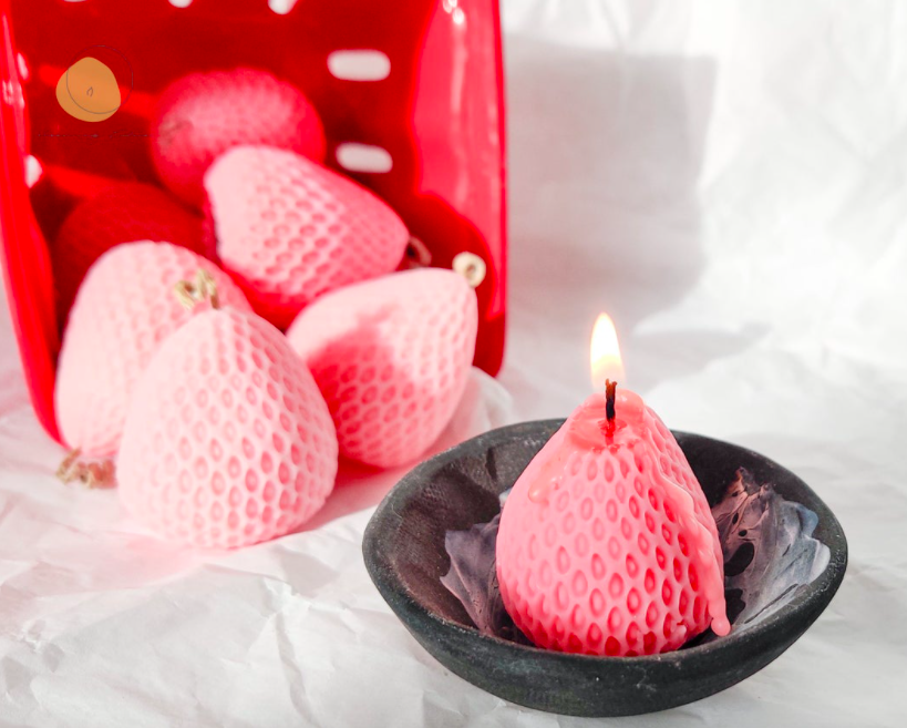 A burning strawberry-shaped candle in a ceramic saucer