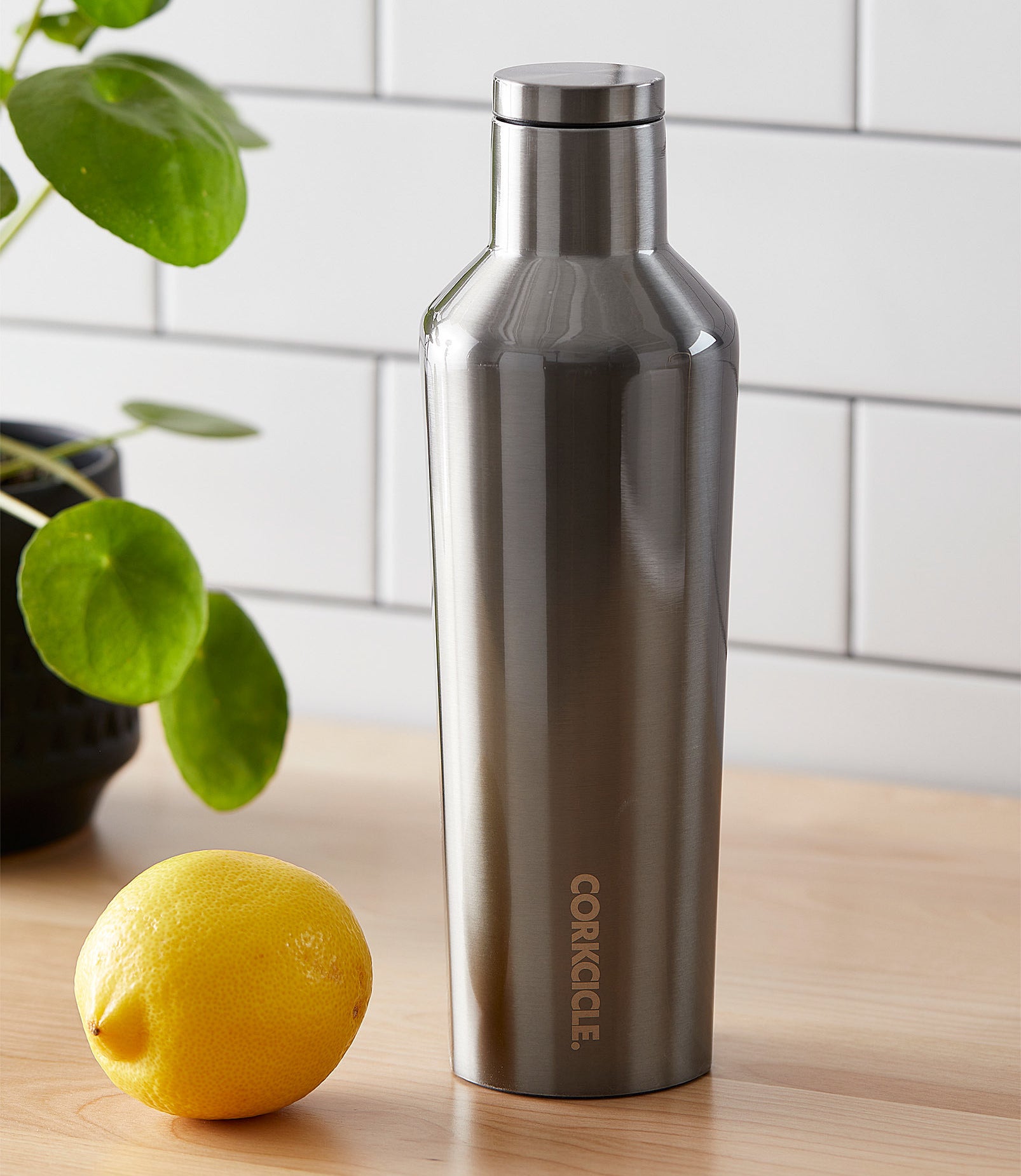 A metallic insulated bottle on a counter next to a lemon
