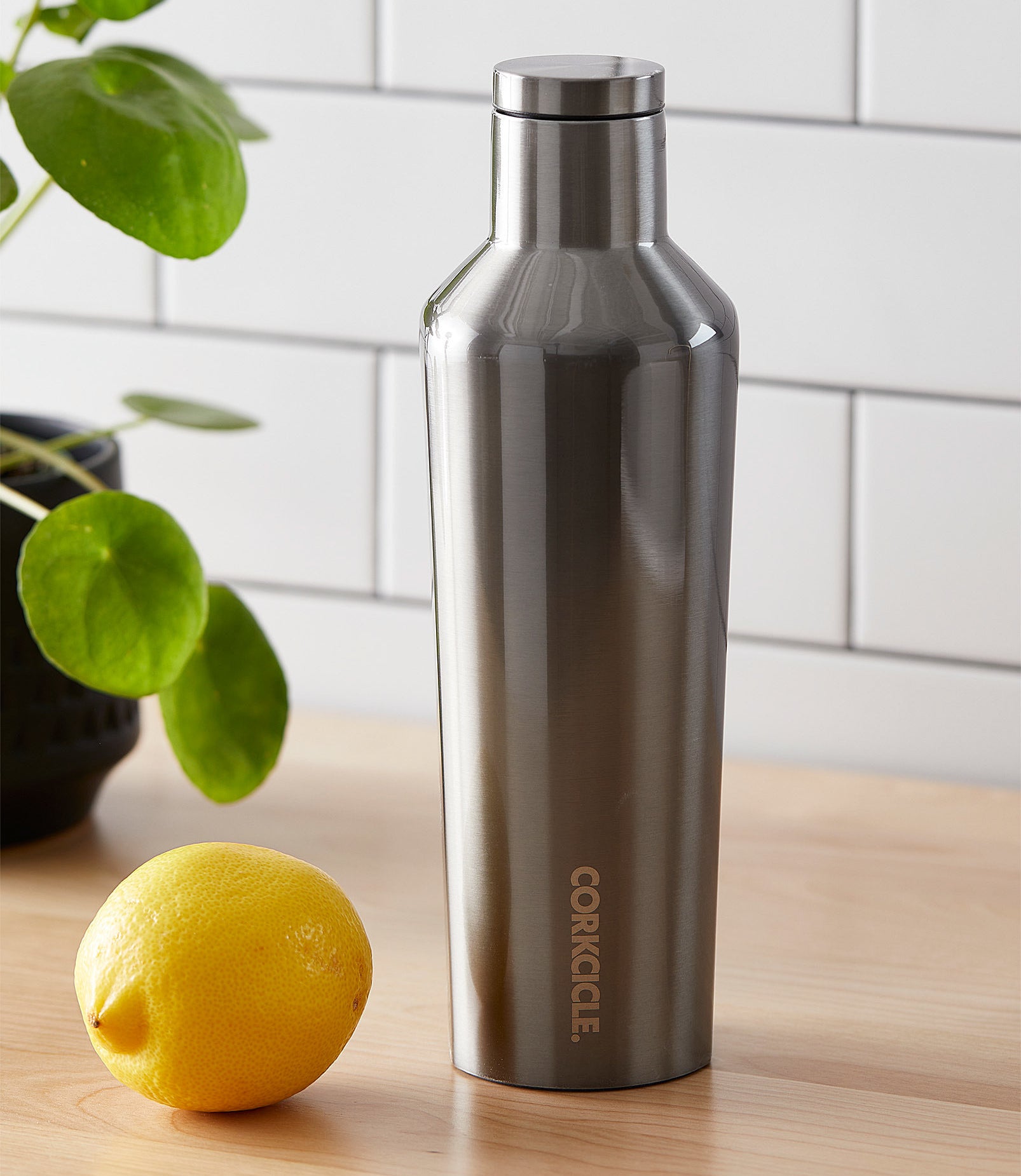 A metallic insulated bottle on a counter next to a lemon