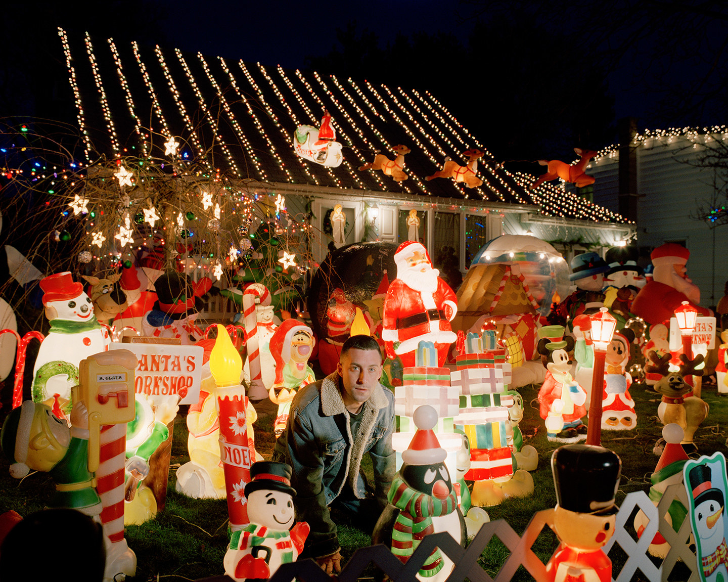 A man surrounded by Christmas ornaments on a lawn in front of a house