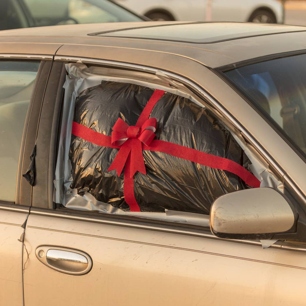 A passenger-side car window is covered in a garbage bag, duct-taped to the vehicle, and decorated with a ribbon and bow