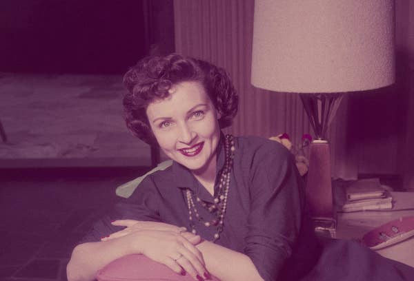 Betty in a navy blue dress leaning on a couch