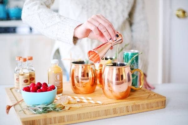A model pouring a shot into a copper mug surrounded by various cocktail ingredients