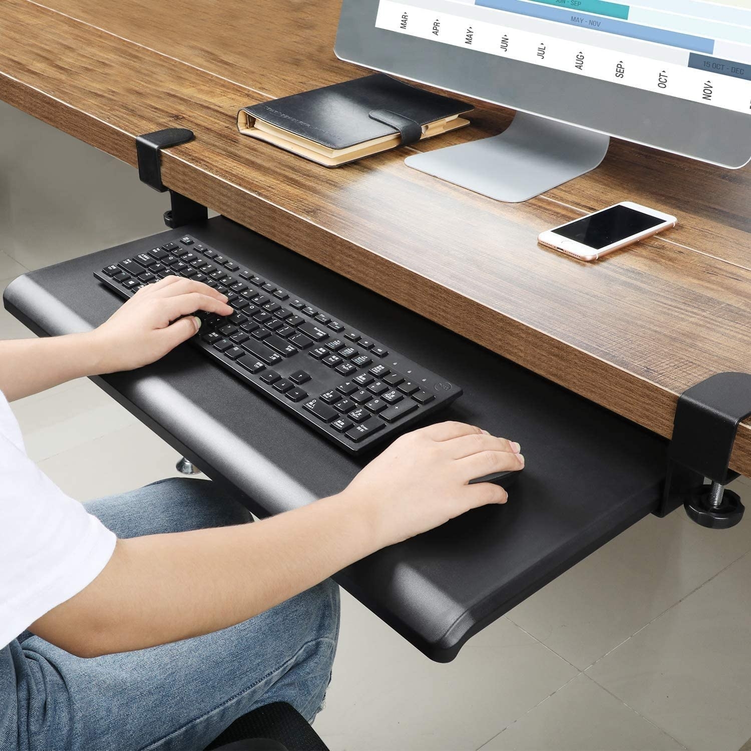 person using a keyboard and mouse on the tray that's clamped to a desk