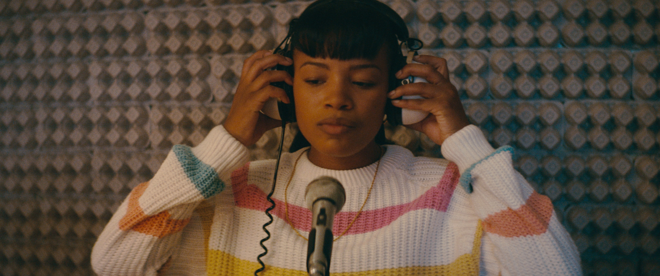 A young Black woman is recording a song in the sound booth of a studio