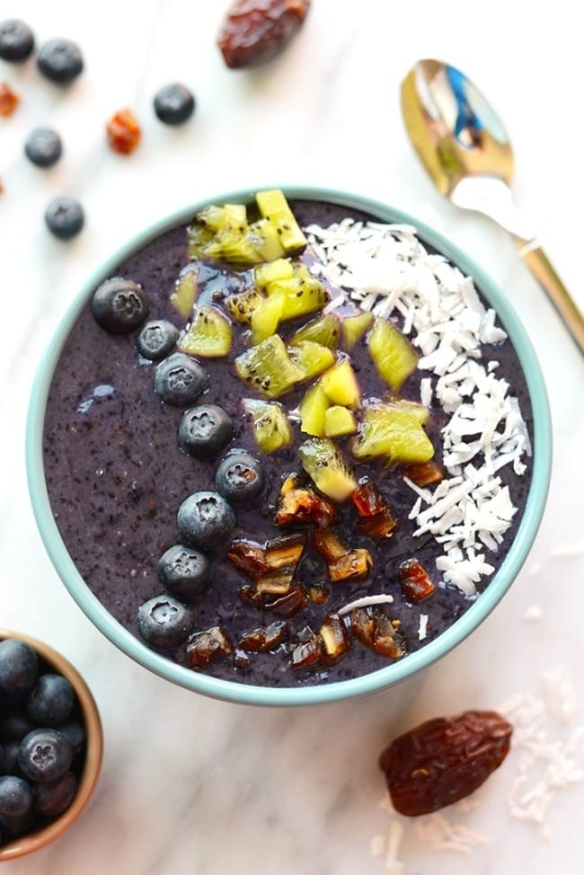 A blueberry smoothie with kiwi, date, and coconut toppings in a bowl