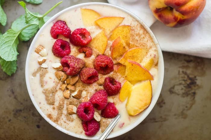 A peach smoothie with raspberry, almond, and peanut butter toppings in a bowl