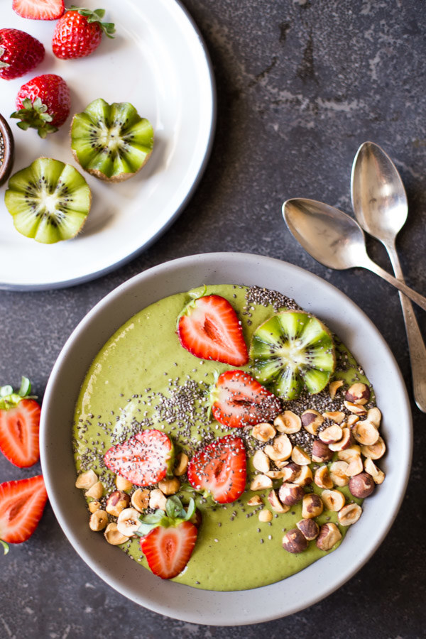 A kiwi smoothie with strawberry and nut toppings in a bowl
