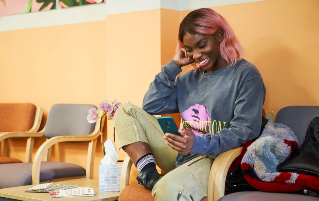 Arabella looks at her phone, smiling, while seated in a waiting room