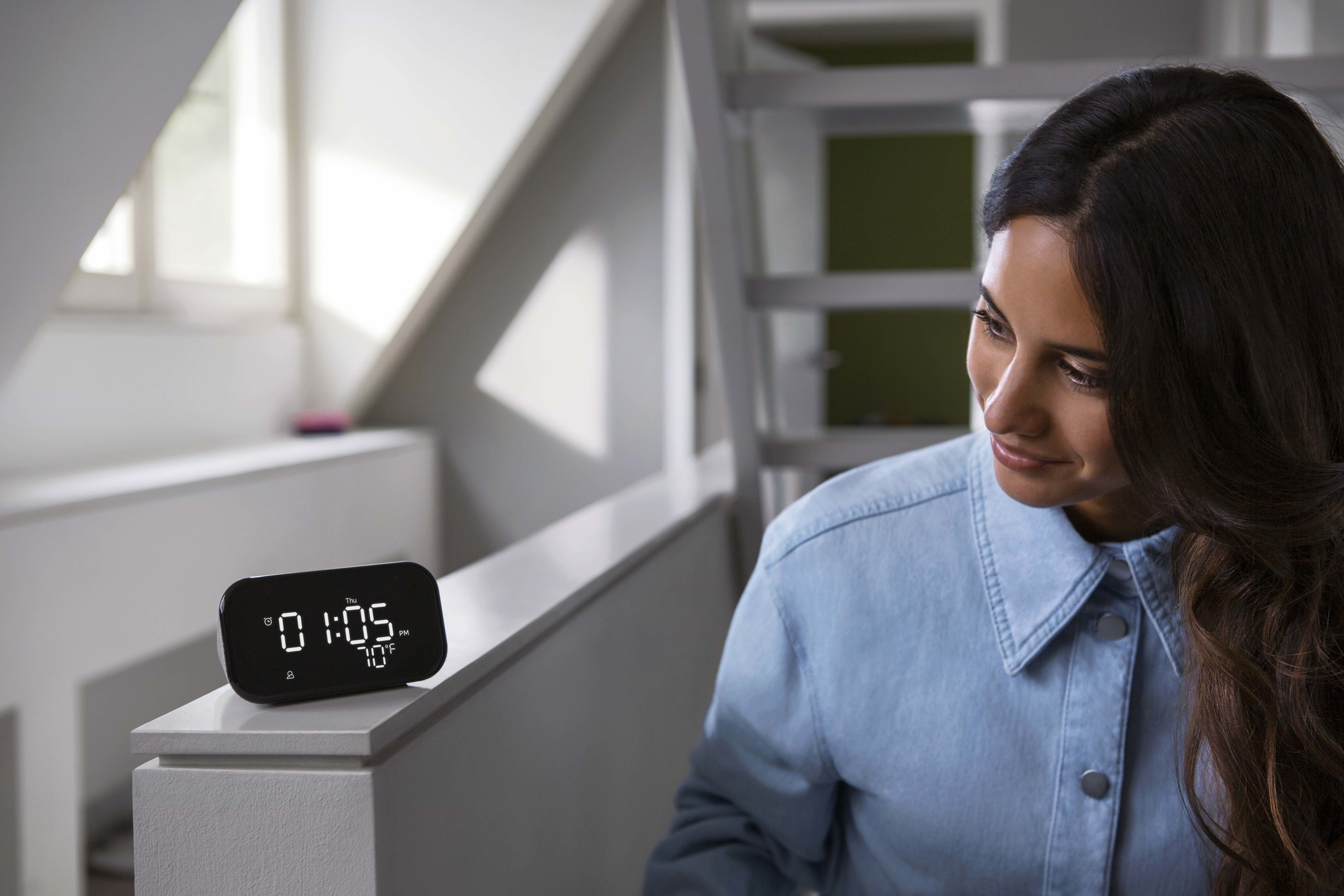 person looking at a lenova smart clock on a white ledge