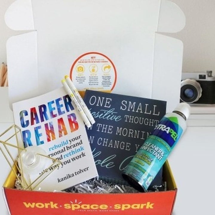 An open box filled with a book titled "Career Rehab", a sign, some pens, and a tech cleaner and disinfectant
