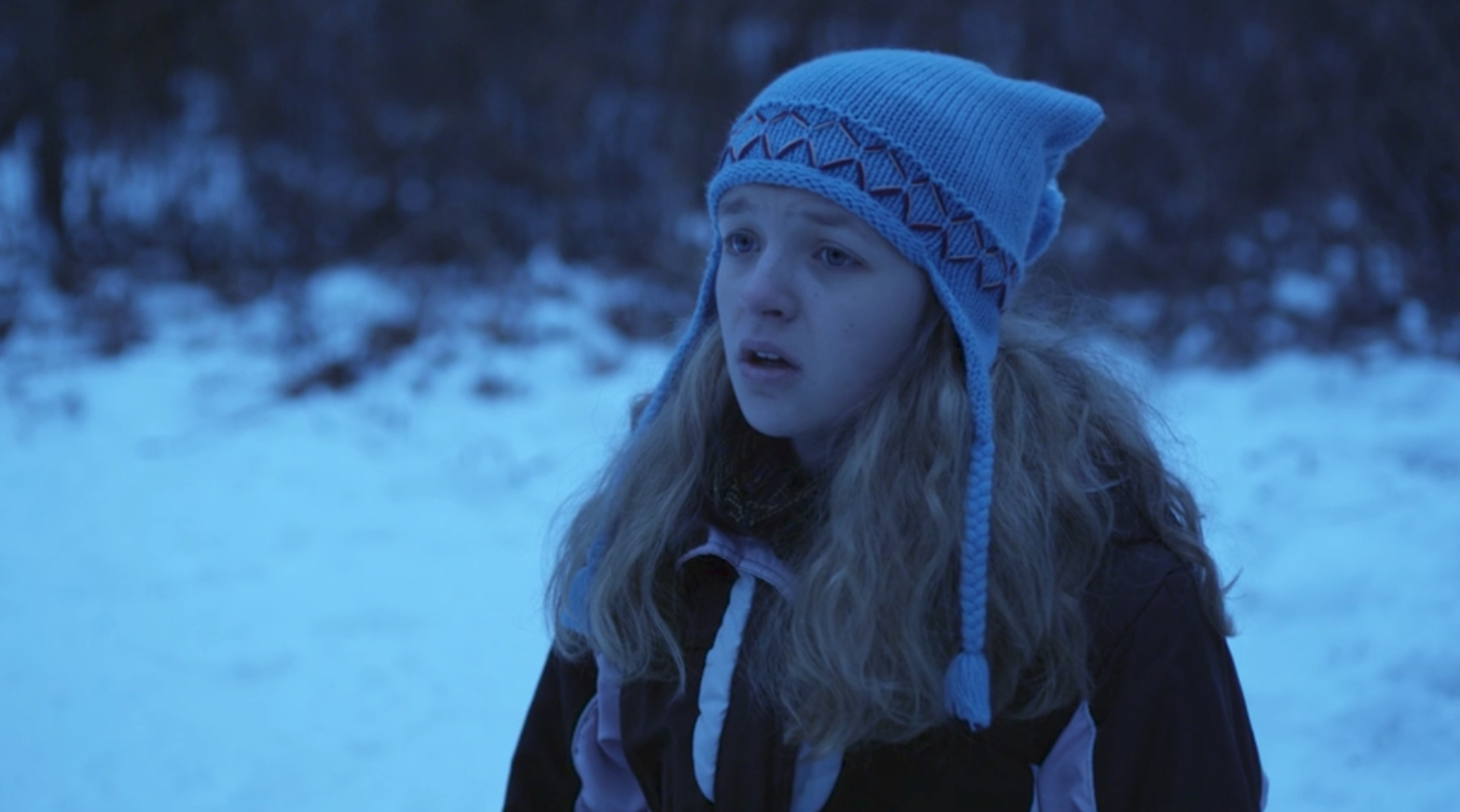 A young woman wears a knitted cap outside in the snow