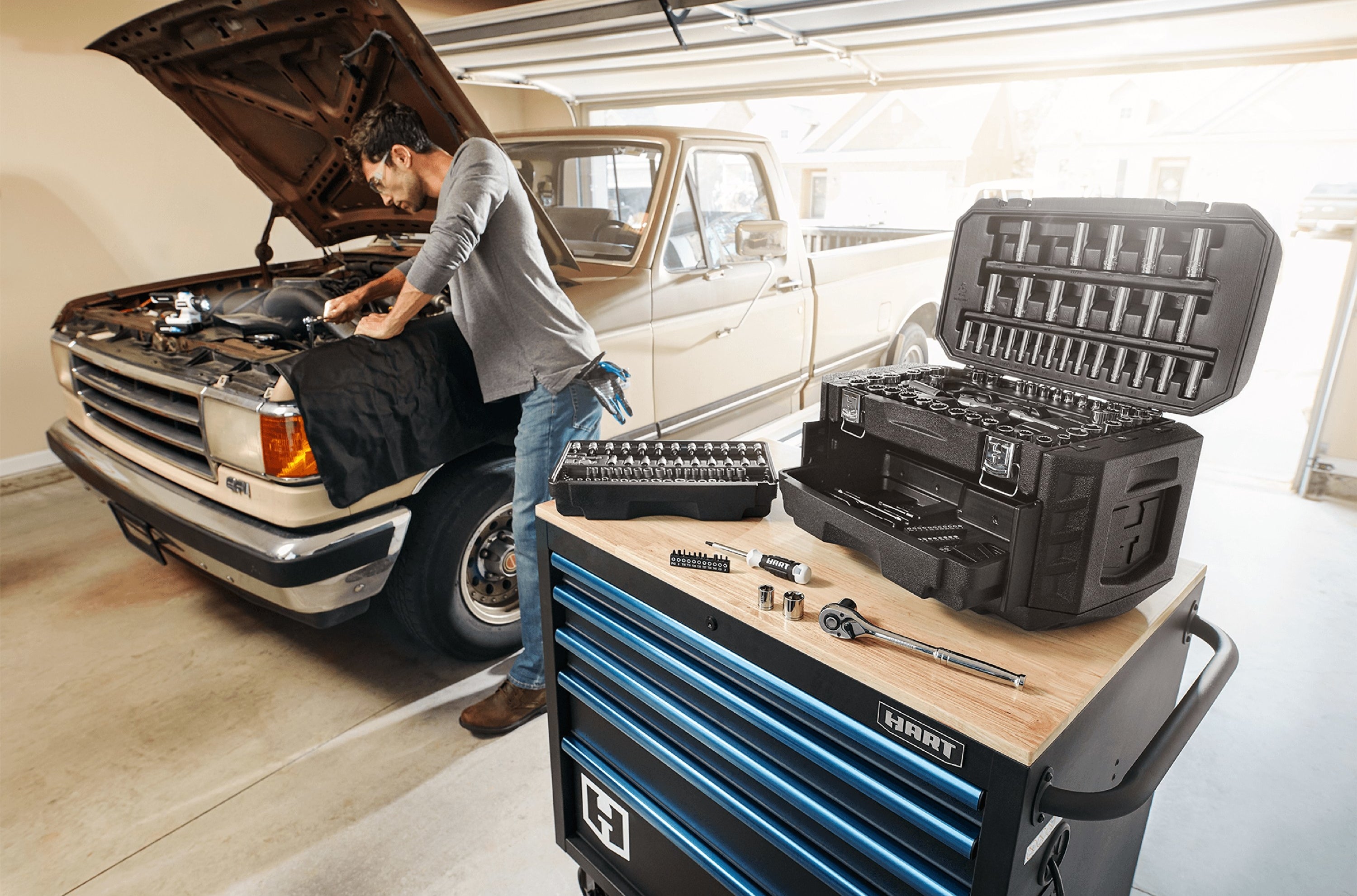 black tool kit with 215 pieces in the foreground with a person working on their car in the background