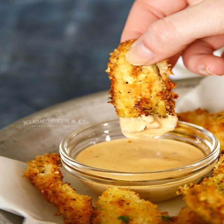 Someone dipping a fried artichoke heart into dipping sauce.