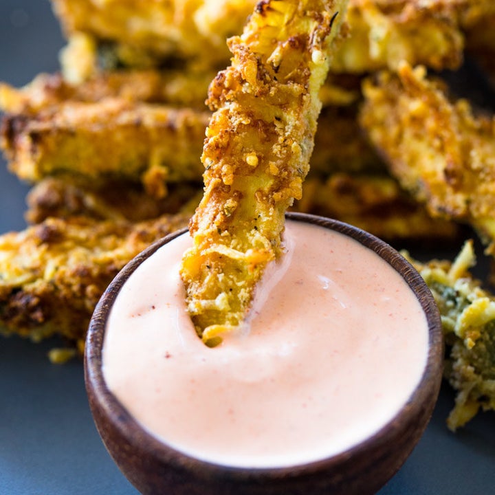 A zucchini fry being dipped into mayo-based sauce.