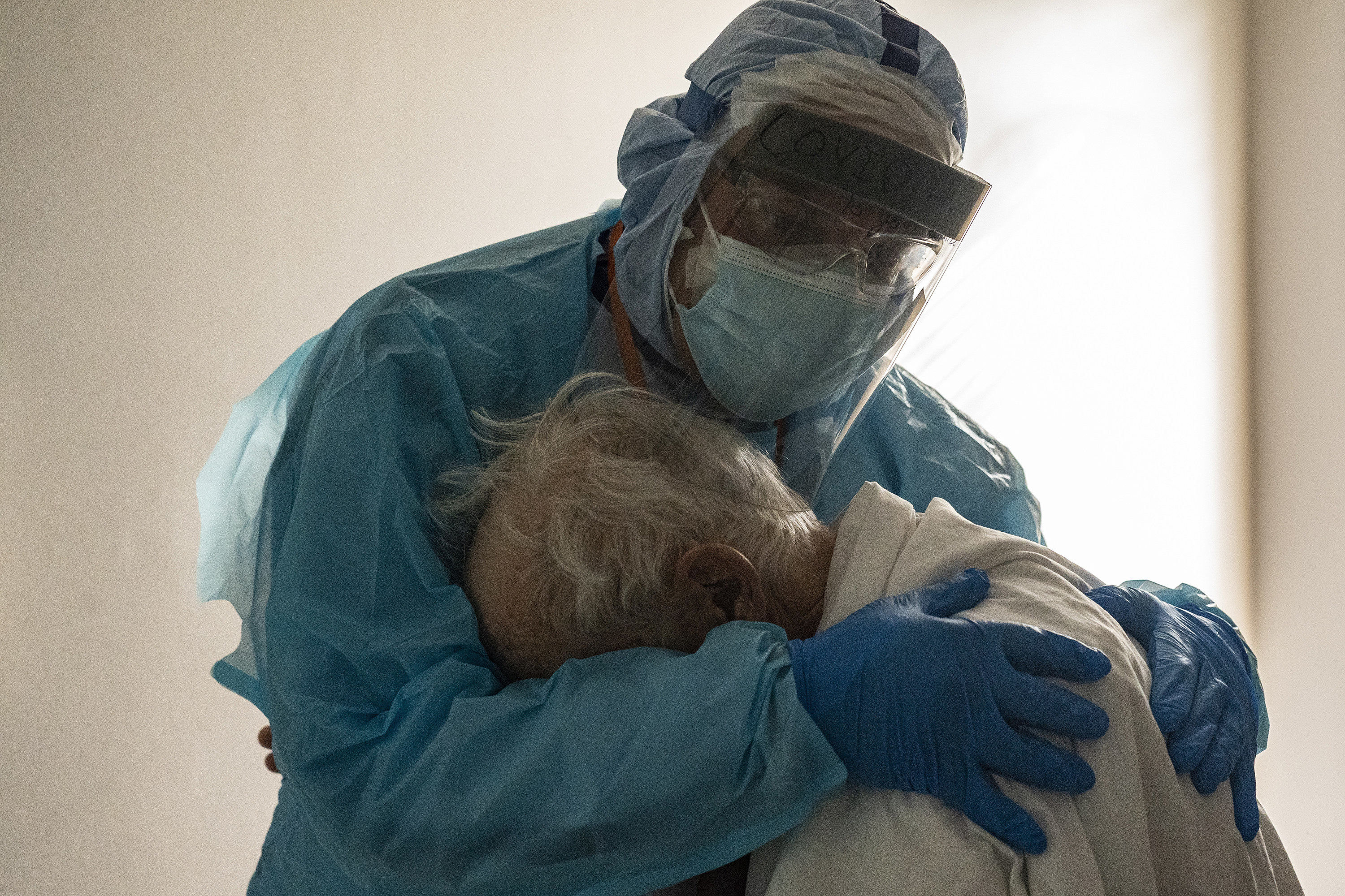 A doctor in full protective gear holds onto a patient and hugs him