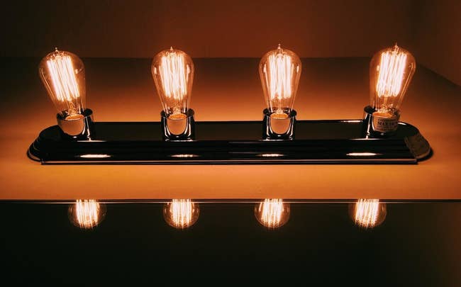 Four vintage-style light bulbs on a fixture, providing warm light, reflected on a surface below