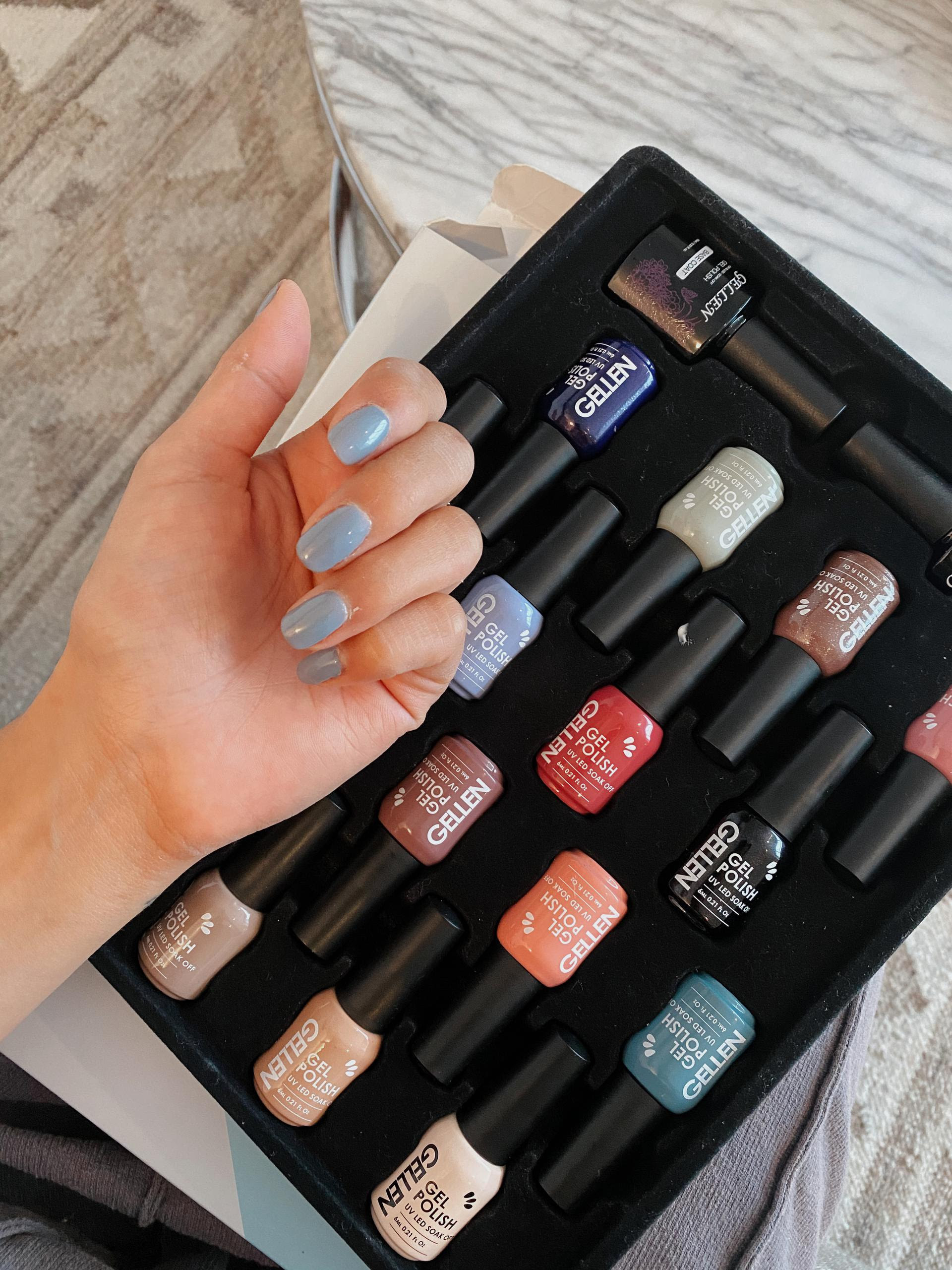 BuzzFeed Editor Kayla Suazo showing the blue gel polish on her nails with the rest of the colors in the set in the background