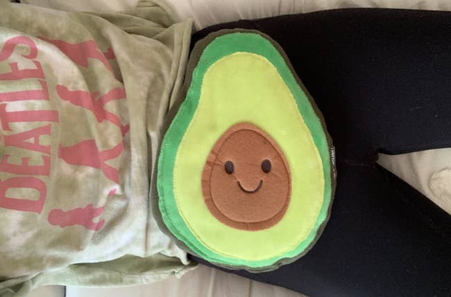 reviewer with the avocado heating pad on their lap