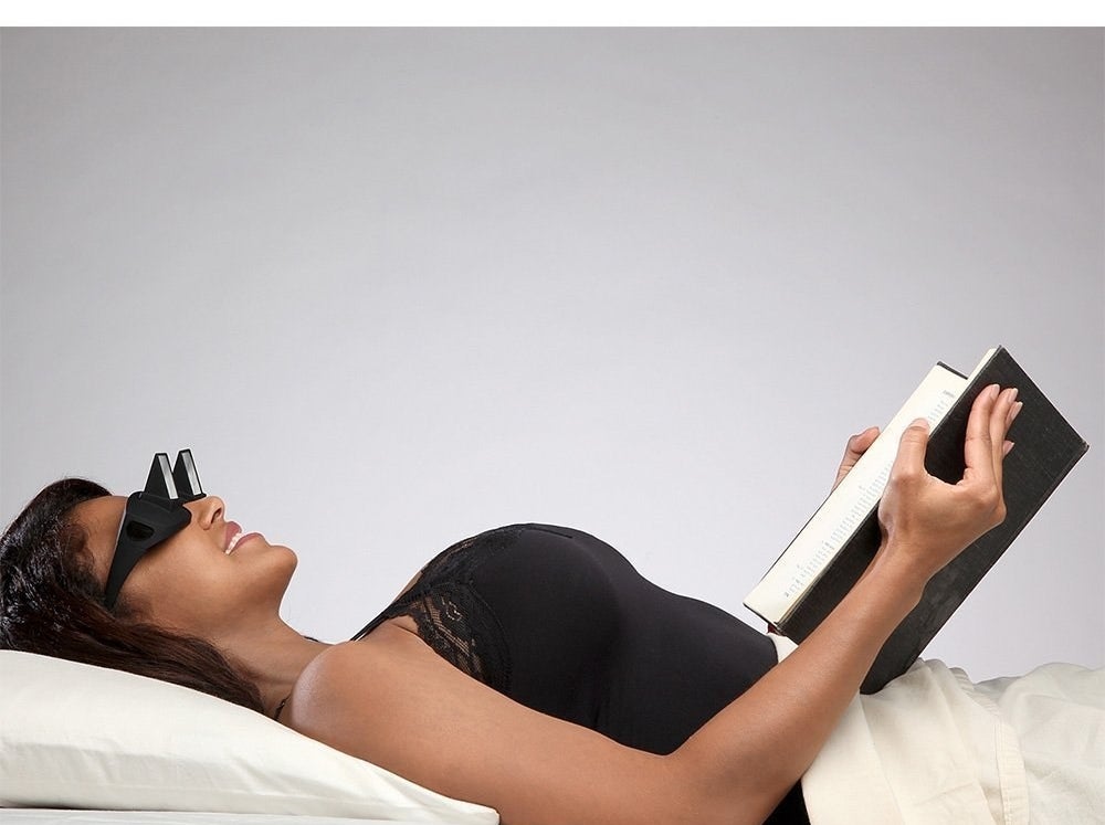 A person lying down while wearing the prism glasses and reading a book.