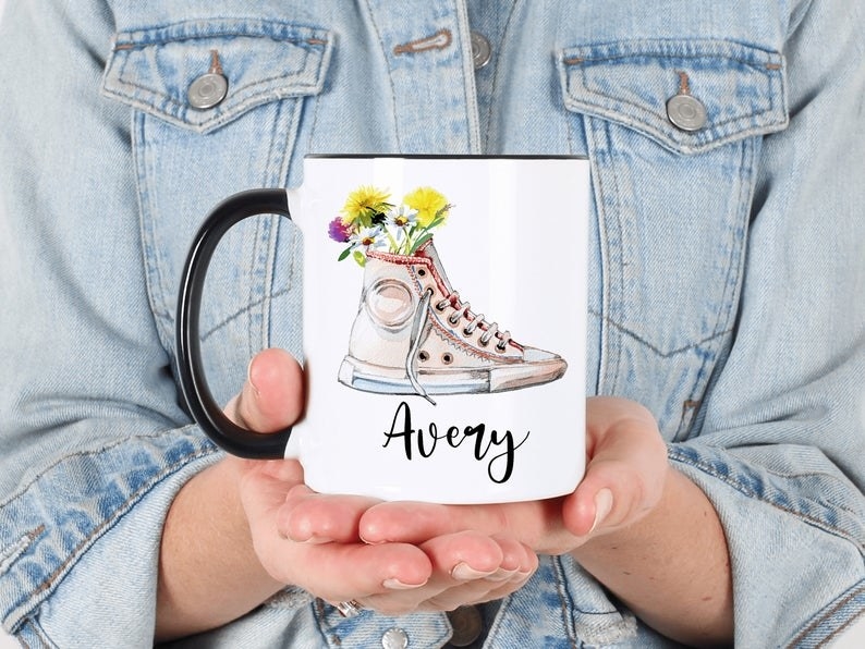 model holding the mug with a converse full of flowers on it and a name in a black cursive