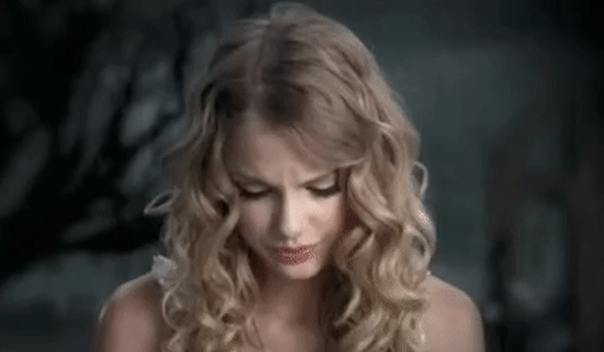a girl with very long curly hair looks down, brows furrowed, mouth pursed. she looks like she is going to cry