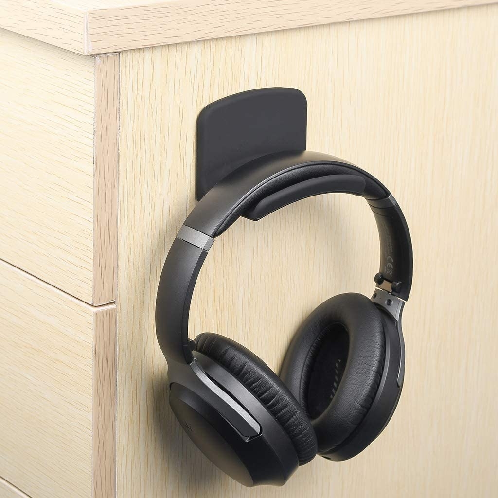 A pair of headphones hanging from a mount stuck to the side of a desk